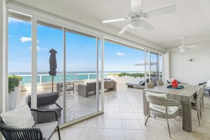 A spacious balcony with a dining area, seating, and a view of the ocean. - Beachfront 3BR Sky Yard | Ocean Views, Pool, WiFi (Seven Mile Beach)