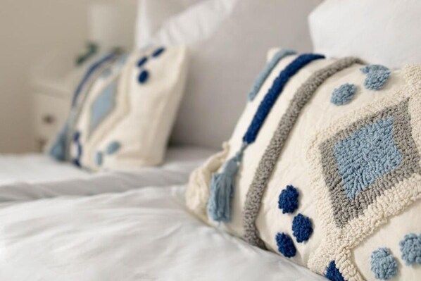 Una cama con ropa blanca y un edredón con motivos azules y beige.