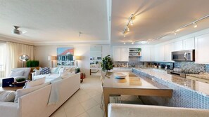 A modern living room with a sofa set, a dining table, and a kitchen area with white cabinets and a microwave.