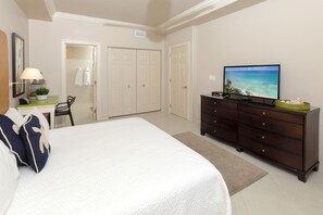A hotel room with a large bed, a desk with a lamp, a dresser, and a television displaying a beach scene.