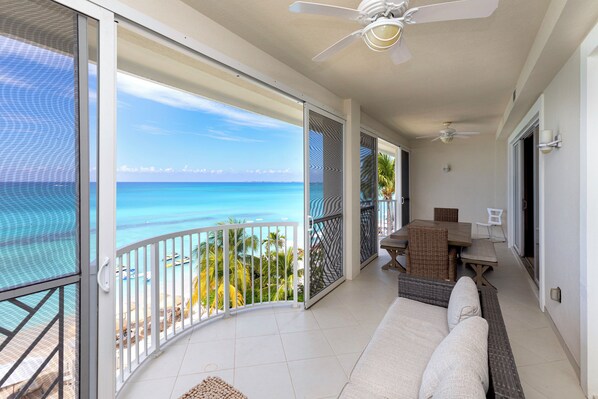 A balcony with a view of the ocean, a ceiling fan, and a seating area with a table and chairs.