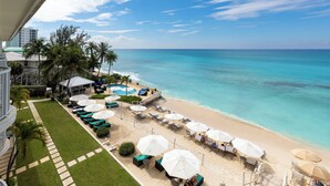 A beachside hotel with a pool, lounge chairs, and umbrellas. - Beachfront 4BR/4BA | Sleeps 10, Ocean Views, Pool (Seven Mile Beach)