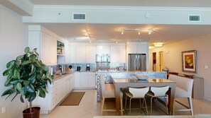 A modern kitchen with white cabinets, a central island, and a dining area with chairs.