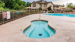 Un bain à remous entouré d’une piscine, avec une clôture et un panneau indiquant qu’il est interdit de fumer et que l’accès est réservé aux adultes.