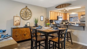 A modern kitchen with wooden cabinets, a dining area with a wooden table and chairs, and a large wall clock. - Branson Escape ~ Pointe Royale Resort Condo ~ Pet Friendly ~ Sleeps 6 (Branson)