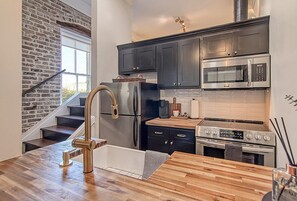 A modern kitchen with dark cabinets, stainless steel appliances, and a wooden countertop. - A Charleston Single - King St. Loft (Charleston)