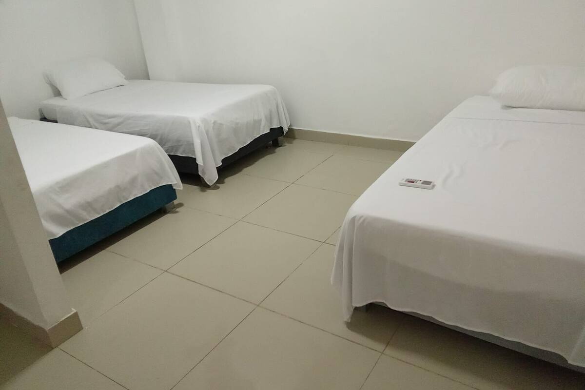 Quarto pequeno e limpo, com duas camas de solteiro, uma parede branca e chão de azulejos.