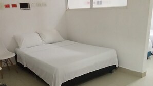 A single-bed room with a white bedspread, a chair, and a small table.