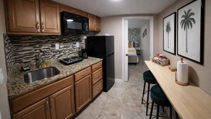 A kitchen with wooden cabinets, a granite countertop, a black refrigerator, and a microwave. There is a sink with a faucet, and a small island with stools. - Guest Suite: Close to Beach & Downtown St. Pete (Pinellas Park)