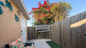 A backyard with a wooden fence, a white lattice structure, and a chair with a floral pattern. - Guest Suite: Close to Beach & Downtown St. Pete (Pinellas Park)