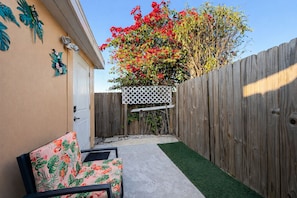 A backyard with a wooden fence, a white lattice structure, and a chair with a floral pattern.