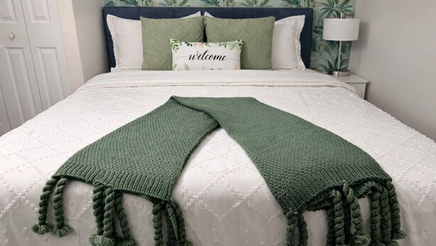 A bed with a white quilt, a green knitted throw, and a 'welcome' pillow. - Guest Suite: Close to Beach & Downtown St. Pete (Pinellas Park)