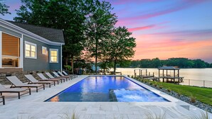 A swimming pool with lounge chairs, a covered area, and a view of a lake at sunset. - Beautiful 5 Bedroom Lake-Front Home with Heated Saltwater Pool, Spa, and Dock (Denver)