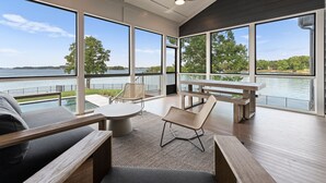 A modern outdoor seating area with a view of a lake, featuring a round table, chairs, and a wooden bench. - Beautiful 5 Bedroom Lake-Front Home with Heated Saltwater Pool, Spa, and Dock (Denver)