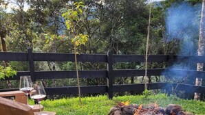 A wooden deck with a fire pit, surrounded by a wooden fence and lush greenery. - Chalet in the middle of the icy mountains of Urubici- (Urubici)
