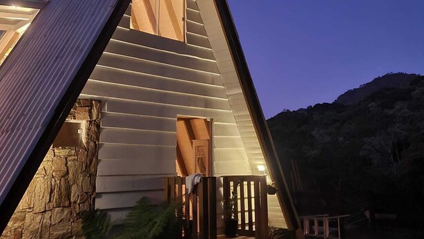 A triangular-shaped building with a stone foundation, a wooden deck, and a large window at the top. - Chalet in the middle of the icy mountains of Urubici- (Urubici)