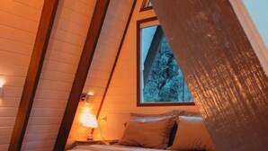 A cozy bedroom with a sloped ceiling, a bed with pillows, a fluffy throw blanket, and a window with a view of trees. - Chalet in the middle of the icy mountains of Urubici- (Urubici)