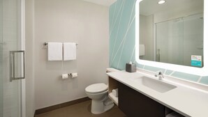 A modern bathroom with a glass shower enclosure, a white toilet, and a vanity with a large mirror. - avid hotel Plano North by IHG (Plano)