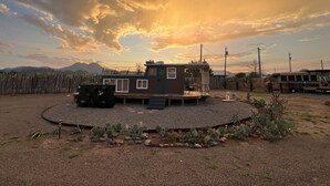 A small, single-story cabin with a deck, surrounded by a gravel area and cacti, set against a sunset sky. - Romantic Houseboat with out of this World Star Gazing (Alpine)