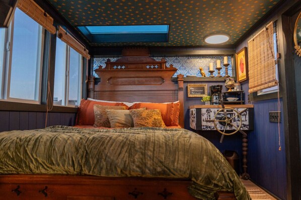 A cozy bedroom with a large bed, a wooden headboard, and a small desk with a lamp and decorative items.