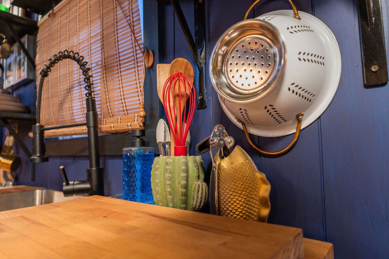 A kitchen with a wooden table, a hanging colander, and various utensils.