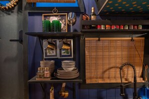 A kitchen with a blue wall, shelves with kitchenware, a framed picture, and a bamboo blind.