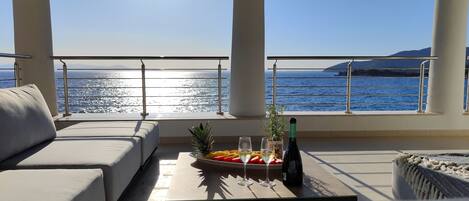 A balcony with a sofa, a table with fruits and drinks, and a view of the sea.