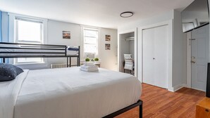 Une chambre avec un lit superposé, une table de chevet avec une lampe, un radiateur et une fenêtre avec des stores.