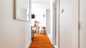 Un couloir étroit avec un plancher en bois, des murs blancs et un coin repas comprenant une table et des chaises.