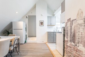 A modern kitchen with white cabinets, a dining area with a table and chairs, and a large abstract painting on the wall.