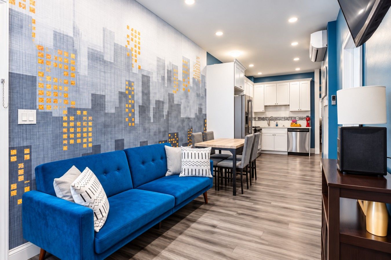 Ein modernes Wohnzimmer mit einem blauen Sofa, einem Esstisch und einer Küche im Hintergrund.