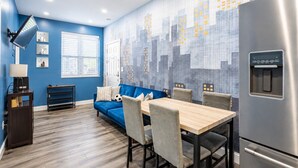 Una cocina moderna con pared azul, un refrigerador de acero inoxidable, una mesa de comedor con sillas y un sofá azul.