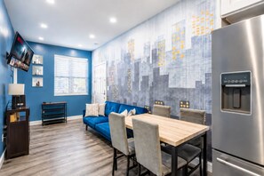 Una cocina moderna con pared azul, una mesa de comedor, sillas, un sofá, un televisor y un refrigerador.