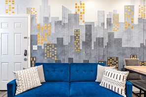 Un sofá azul con almohadones estampados en una habitación con un mural de paisaje urbano.
