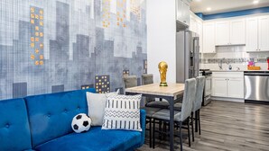 A modern kitchen with white cabinets, a stainless steel dishwasher, and a dining area with a blue sofa and a soccer ball.