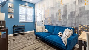 Una sala de estar moderna con un sofá azul, una mesa de centro de madera y un mural con un paisaje urbano en la pared.