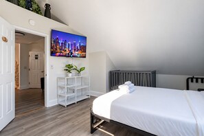 A modern bedroom with a bed, a TV mounted on the wall, a white console table with plants, and a radiator.