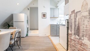 Eine moderne Küche mit weißen Schränken, einem Essbereich mit Tisch und Stühlen sowie einem großen, abstrakten Gemälde an der Wand.