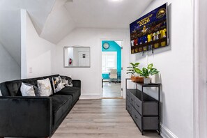 Un salon moderne avec un canapé noir, une table basse, un téléviseur fixé au mur et une plante posée sur une table d’appoint.
