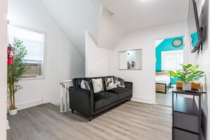 En moderne stue med en sort sofa, et lille bord, et spejl og en potteplante.