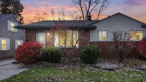 A two-story house with a brick facade, multiple windows, and a well-maintained front yard with shrubs and a lawn. - CHARMING HOUSE ON THE NAUTICAL MILE (St. Clair Shores)
