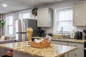A kitchen with granite countertops, a refrigerator, a coffee maker, and a basket of snacks.