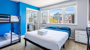 Une chambre avec un lit superposé, un lit simple, une fenêtre donnant sur la ville et une commode blanche.