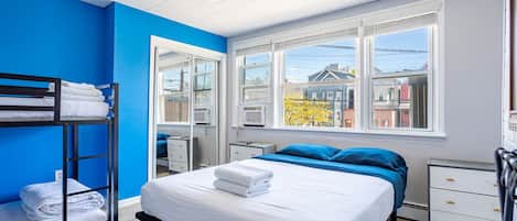 A bedroom with a bunk bed, a single bed, a window with a city view, and a white dresser.
