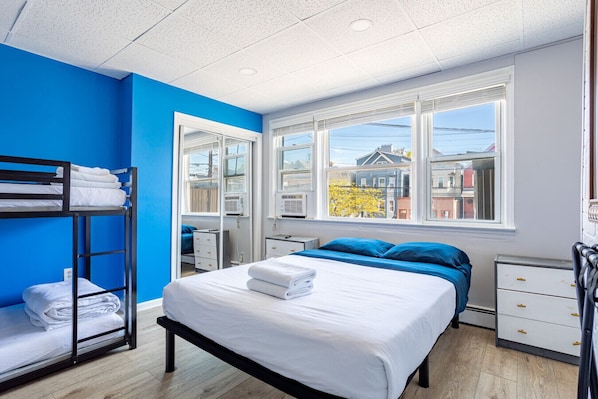 Ein Schlafzimmer mit einem Etagenbett, einem Einzelbett, einem Fenster mit Blick auf die Stadt und einer weißen Kommode.