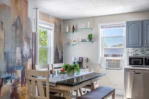 A kitchen with a dining table, chairs, a microwave, an oven, and a glass shelf with decorative items.
