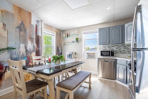 A modern kitchen with a dining table, chairs, and a refrigerator.