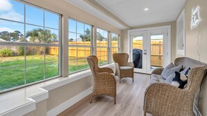 Une pièce spacieuse avec de grandes fenêtres, des meubles en osier et une vue sur un jardin.