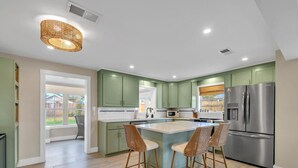 Une cuisine moderne avec des meubles de couleur verte, un réfrigérateur en acier inoxydable et un îlot central doté de tabourets de bar.