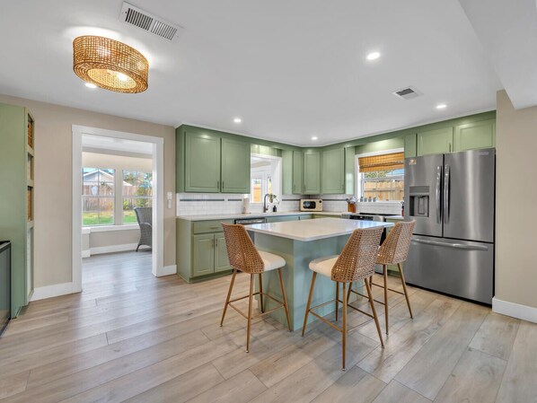 A modern kitchen with green cabinets, a stainless steel refrigerator, and a central island with bar stools.